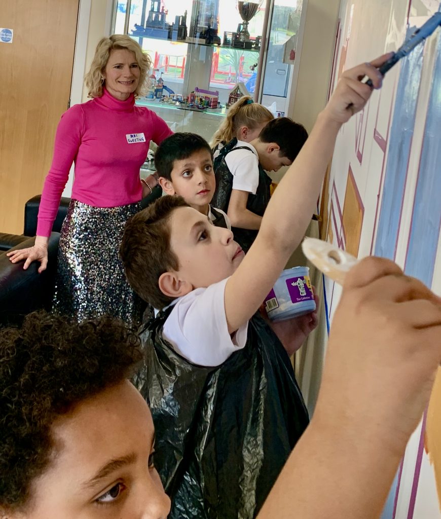 Female artist in residence at Pioneer Educational Trust watches as schoolchildren paint a wall mural.